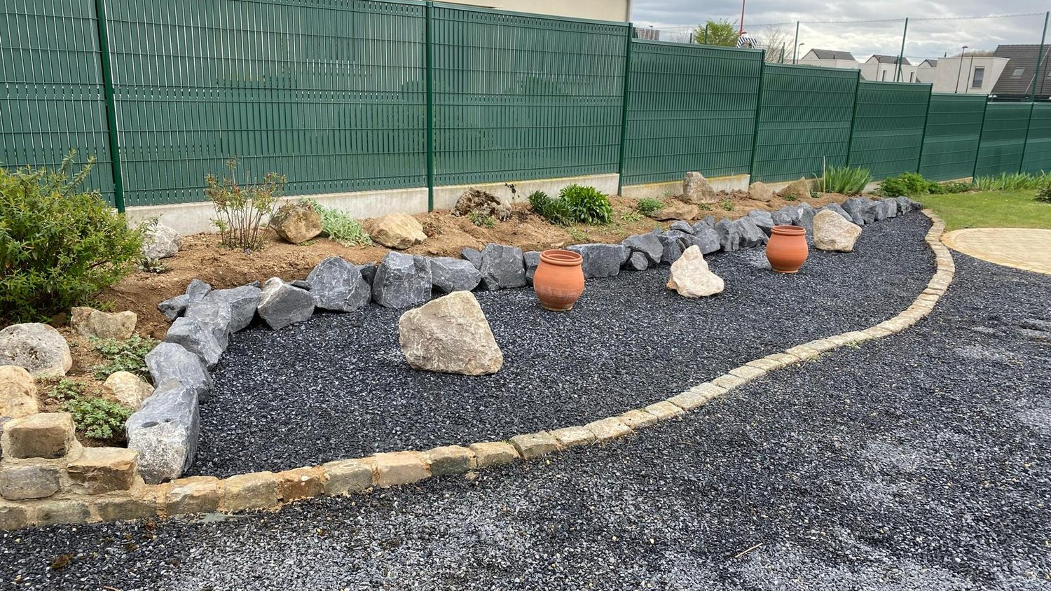 Massif aménagé en rocaille avec galets, plantes et allée gravier